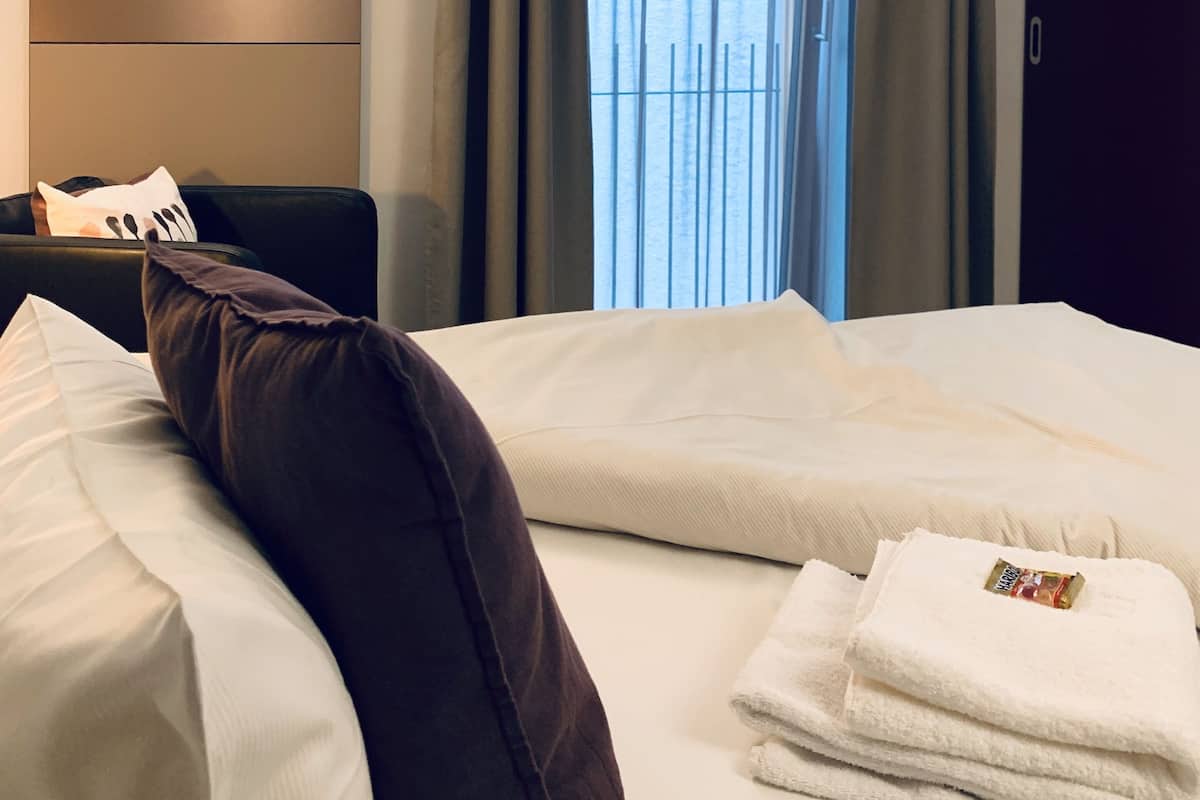 Une chambre d’hôtel avec un lit, une table de chevet, une lampe et une fenêtre avec des rideaux.