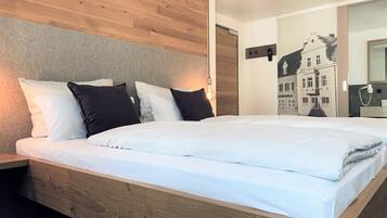 Een moderne slaapkamer met een houten hoofdbord, een groot bed met wit beddengoed en een muurschildering van een stadsgezicht.