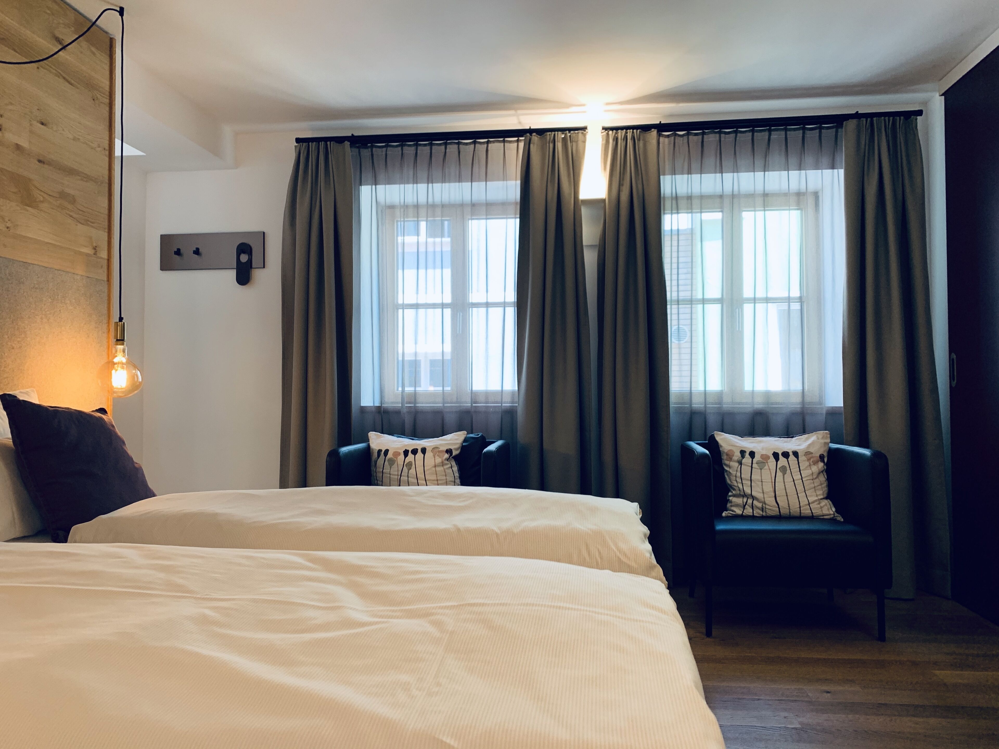 Een hotelkamer met twee bedden, een houten hoofdbord, een wandlamp en een raam met gordijnen.