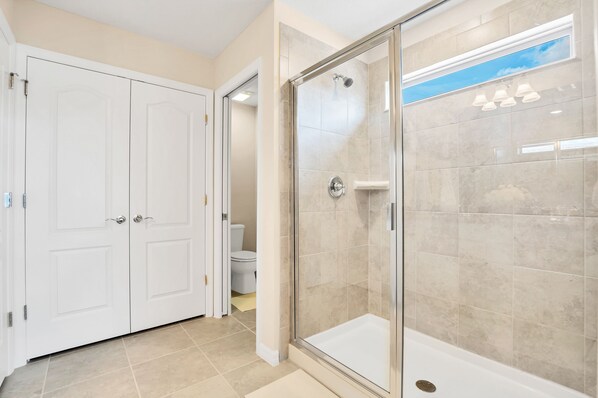 Une salle de bain avec une douche à parois de verre, des murs recouverts de carreaux blancs et des toilettes blanches.