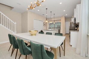 A spacious kitchen with white cabinets, a large island, and a dining area with a white table and green chairs.