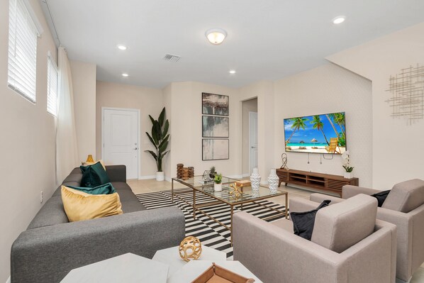 A modern living room with a sofa, coffee table, and a flat-screen TV mounted on the wall. - Private Pool & Spa • Spacious TV Loft • Gated Resort Waterslides • Near Disney (Davenport)