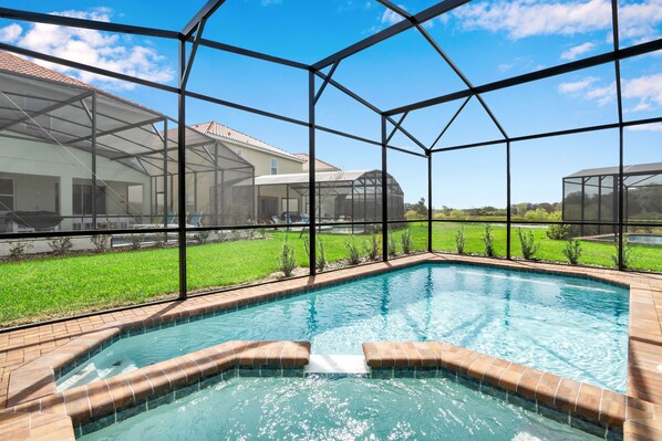 A swimming pool with a glass enclosure, surrounded by a grassy area and a house.