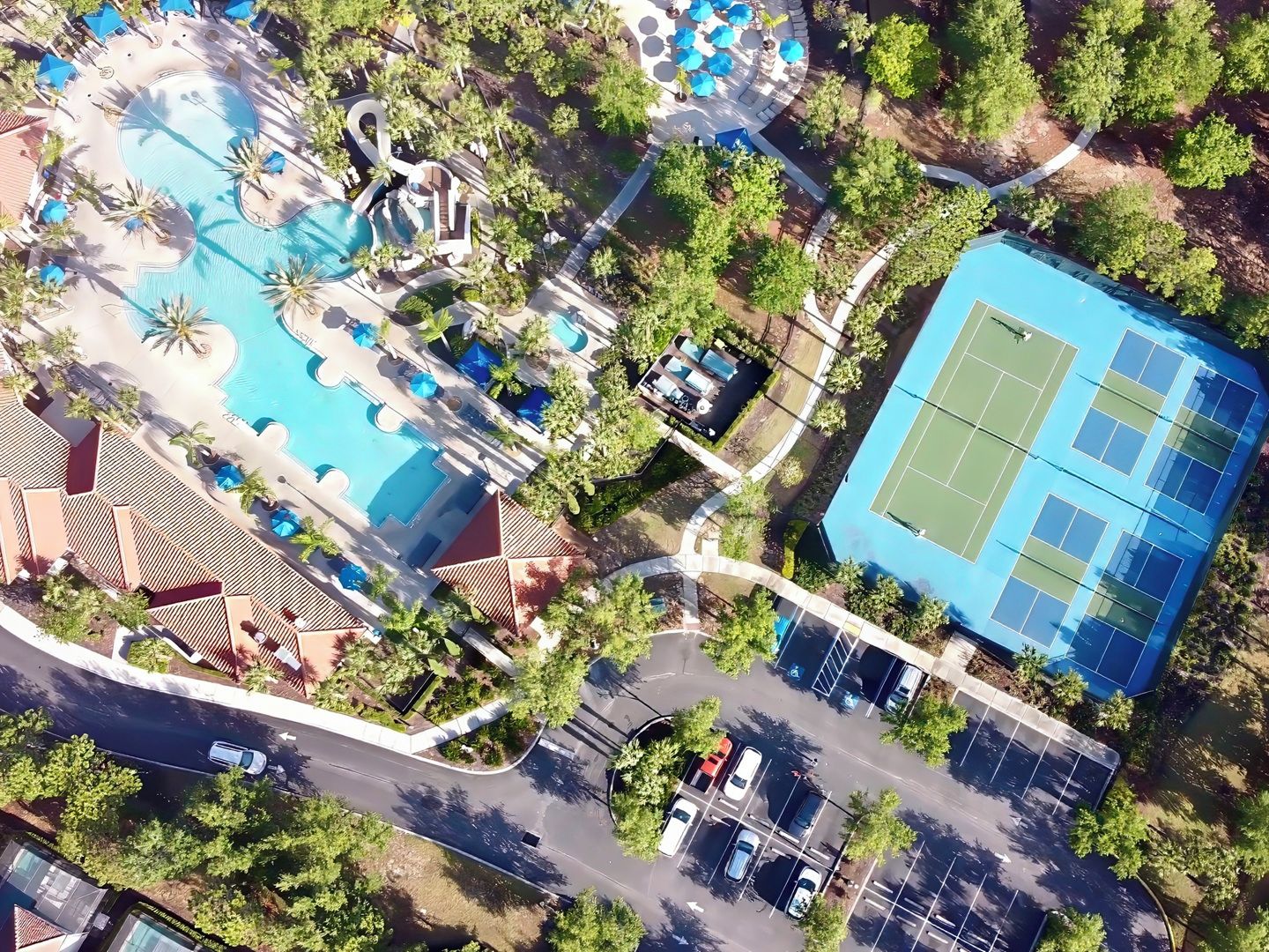 Vue aérienne d’un complexe hôtelier doté d’une piscine, d’un court de tennis et d’un parking.