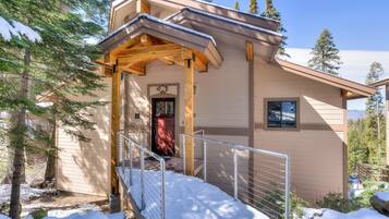 A modern building with a wooden porch, a red door, and a metal railing.