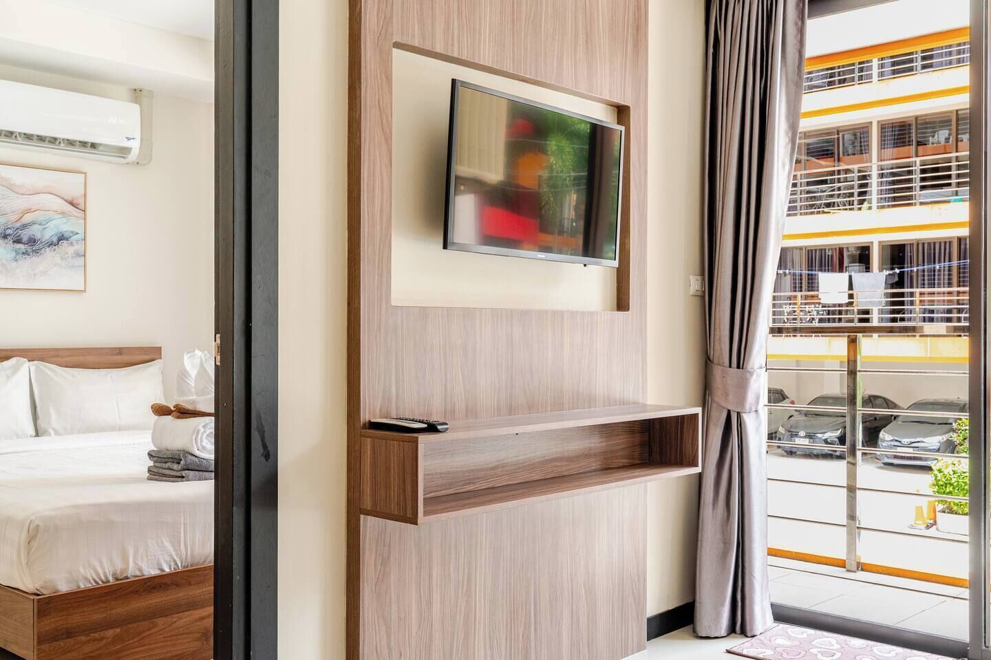 Een moderne hotelkamer met een bed, een wandgemonteerde televisie en uitzicht op een gebouw met een geel en wit gevel.