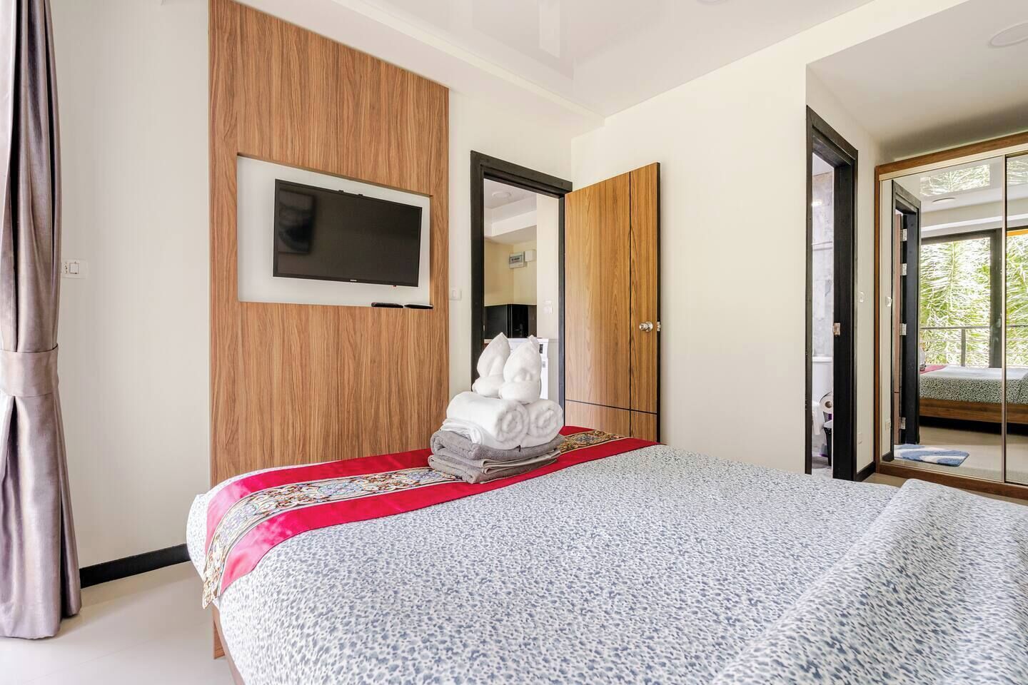 Habitación de hotel con cama, televisor montado en la pared, armario y puerta corrediza de vidrio que da a un balcón.