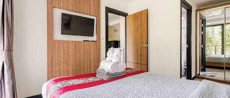 Habitación de hotel con cama, televisor montado en la pared, armario y puerta corrediza de vidrio que da a un balcón.
