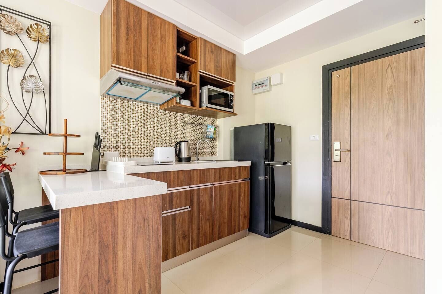 A modern kitchen with wooden cabinets, a black refrigerator, a microwave, and a tiled backsplash.