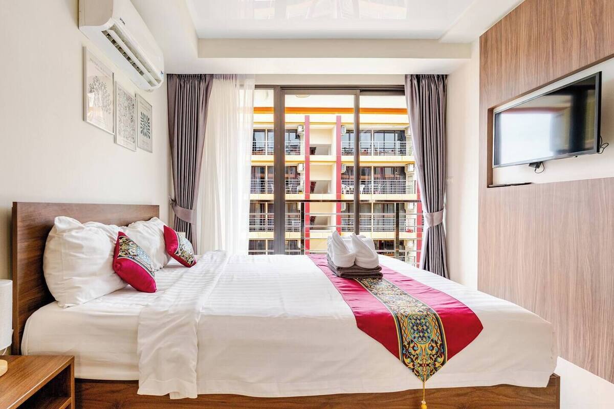 Ein Hotelzimmer mit einem großen Bett, einem wandmontierten Flachbildfernseher und einem Fenster mit Vorhängen.