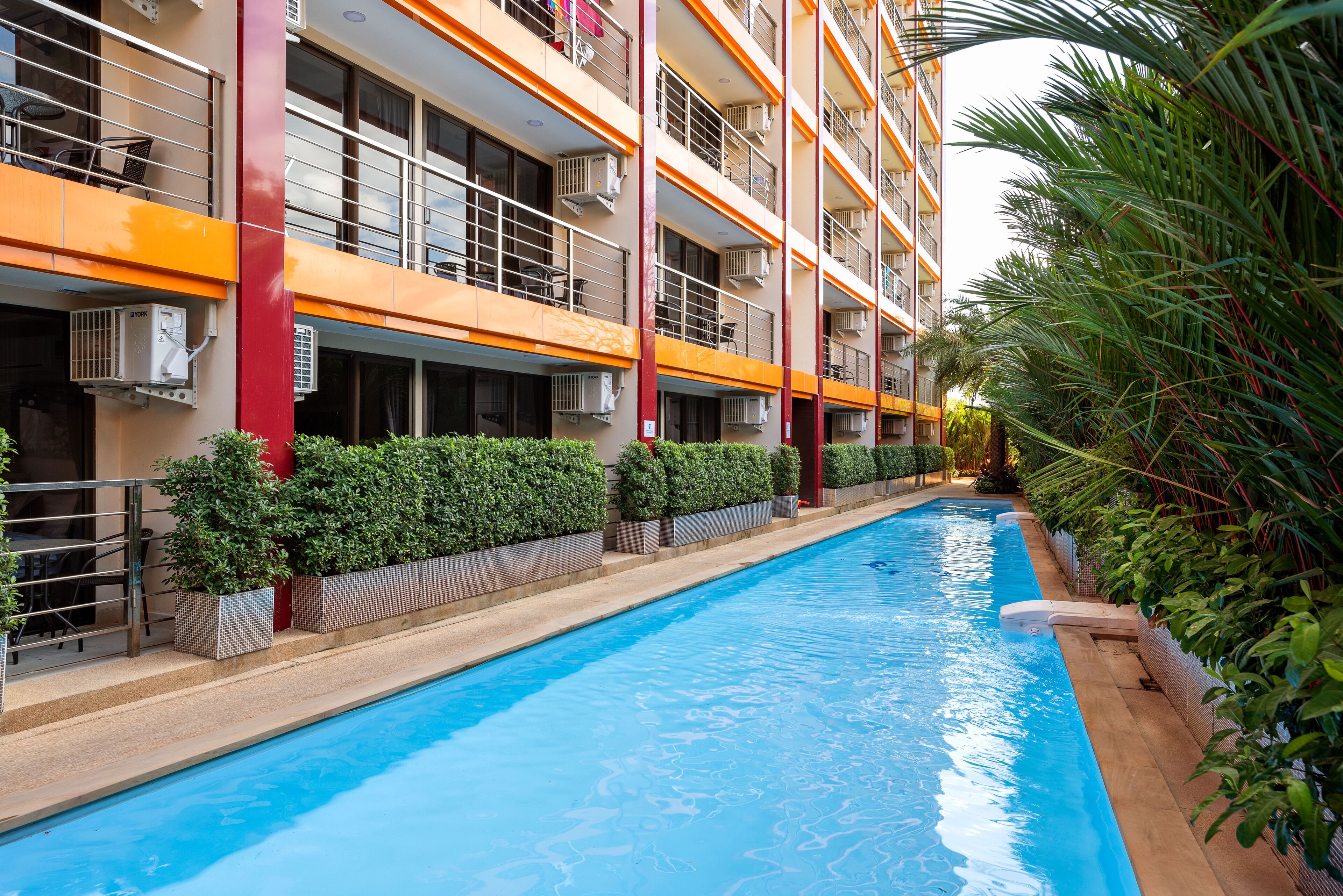 En swimmingpool ved siden af en mangeetagers bygning med altaner, aircondition og plantekasser.