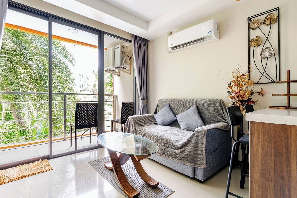Ein modernes Wohnzimmer mit Glastisch, grauem Sofa und einem Balkon mit Blick auf Grünflächen.