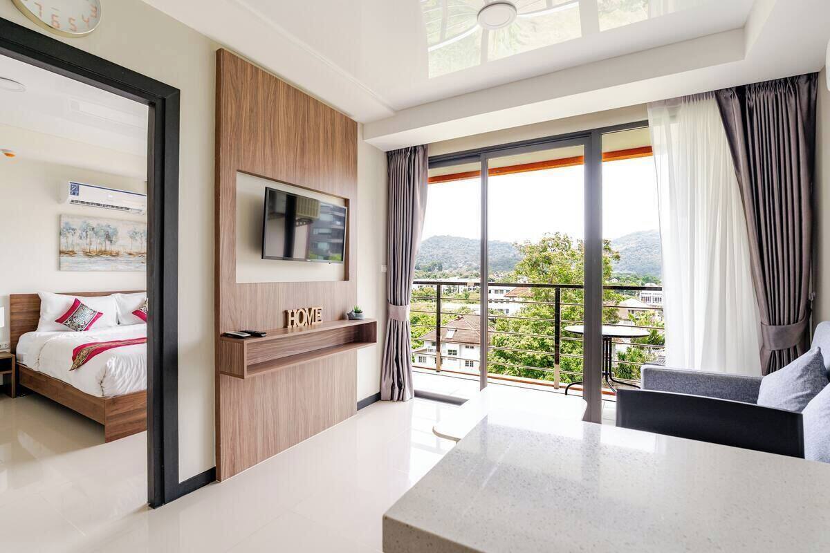 Ein modernes Hotelzimmer mit einem Bett, einem an einer Holzvertäfelung montierten Fernseher, einem Balkon mit Stadtblick und einem Essbereich.