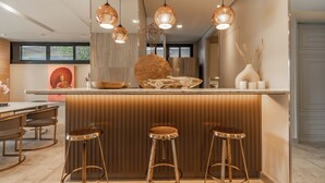 A modern kitchen with a central island, bar stools, pendant lighting, and a large decorative vase.