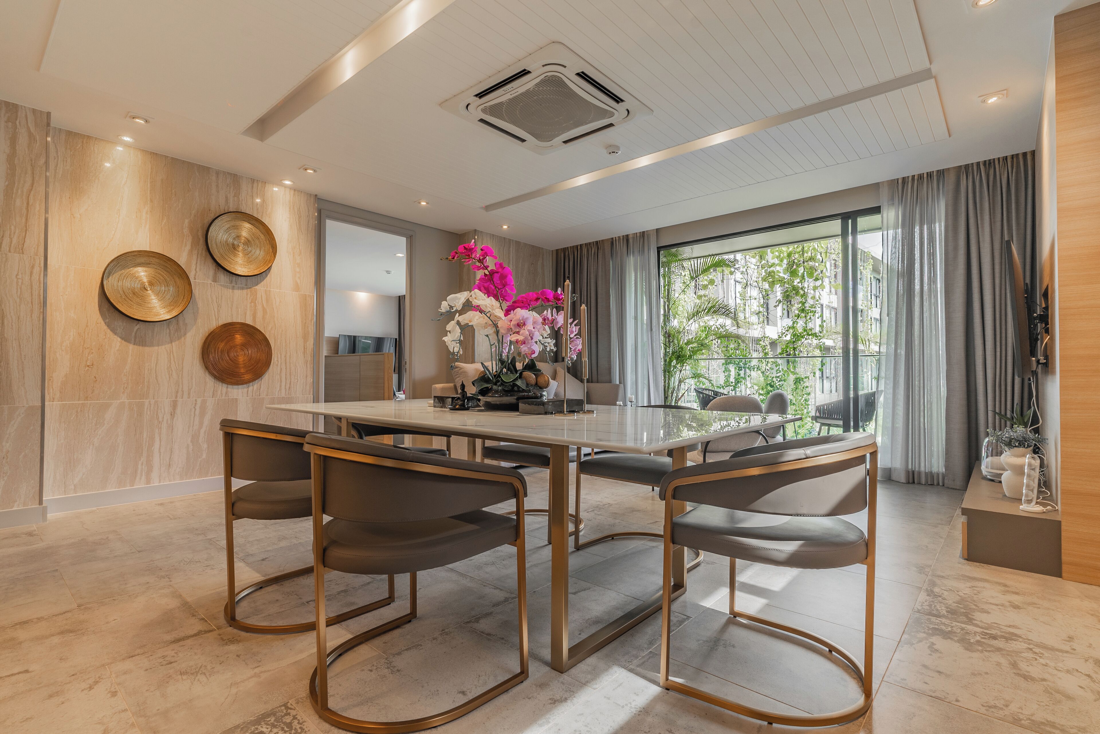 A modern dining area with a large table and four chairs, a decorative wall with circular mirrors, and a view of greenery through large windows.