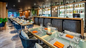 A restaurant with long tables, chairs, and a bar area with shelves of bottles.