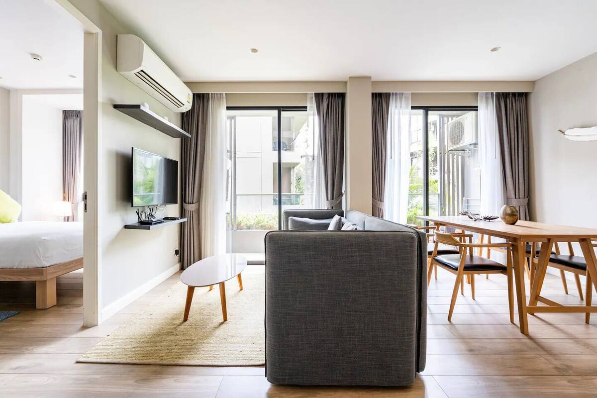 Moderni hotellihuone, jossa on sohva, ruokapöytä, televisio ja suuret ikkunat.