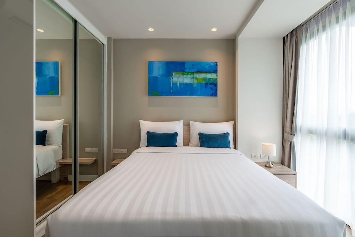 A modern hotel room with a large bed, a glass partition, and a painting on the wall.