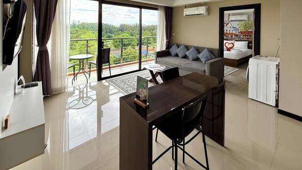 A modern hotel room with a balcony, a sofa, a dining area, and a TV. - Mai Khao Beach Condotel by Villacarte (Mai Khao)