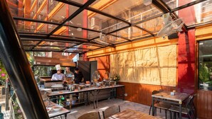 An outdoor dining area with a chef preparing food, a large mural on the wall, and a glass enclosure. - Mai Khao Beach Condotel by Villacarte (Mai Khao)