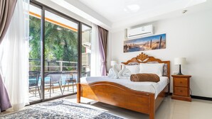 A bedroom with a wooden bed, a view of a swimming pool, and an air conditioning unit on the wall. - Mai Khao Beach Condotel by Villacarte (Mai Khao)