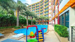 A hotel pool area with a children's play structure, palm trees, and a multi-story building with balconies. - Mai Khao Beach Condotel by Villacarte (Mai Khao)