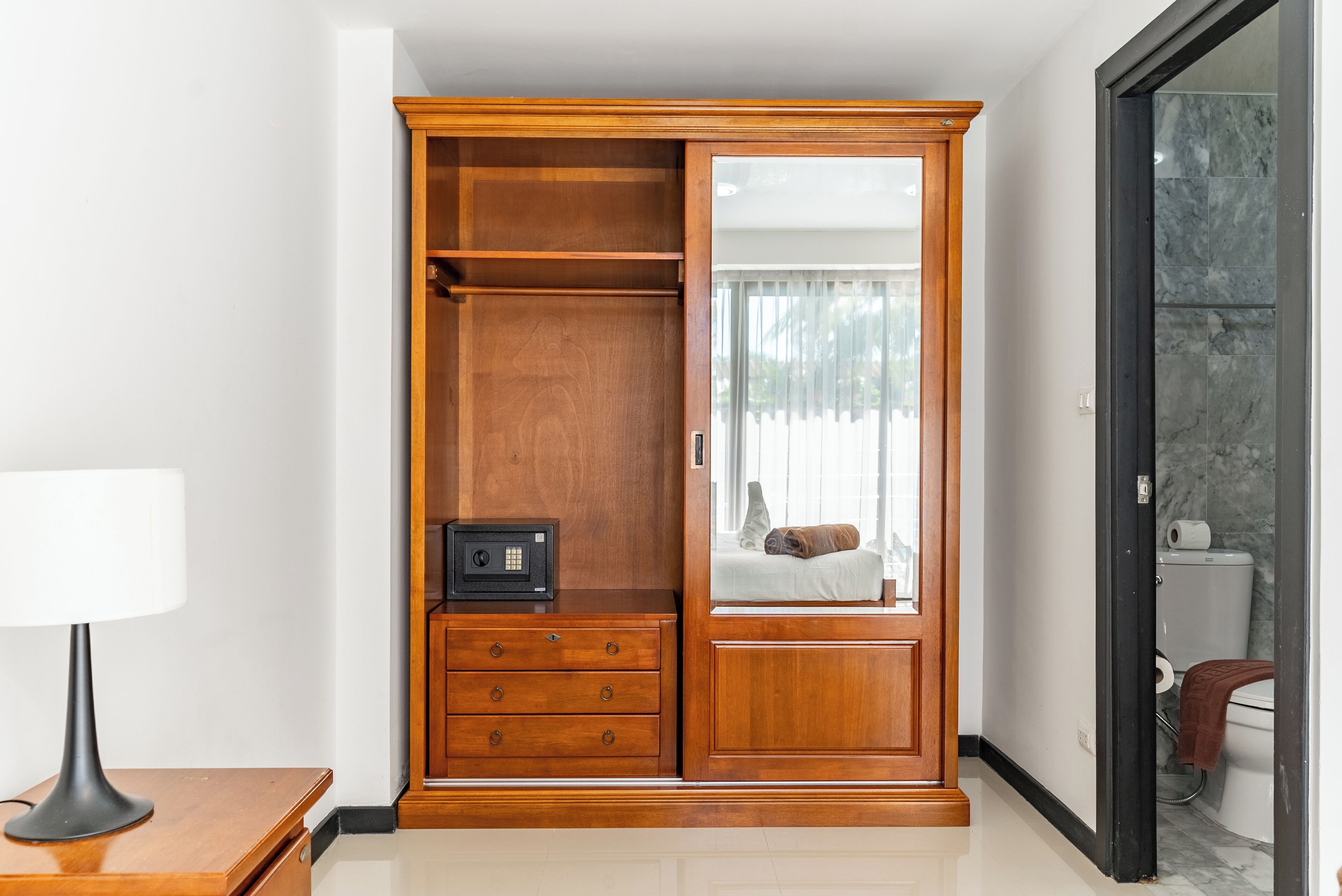 Un armario de madera con espejo, una caja fuerte pequeña y una cama con vistas al exterior.