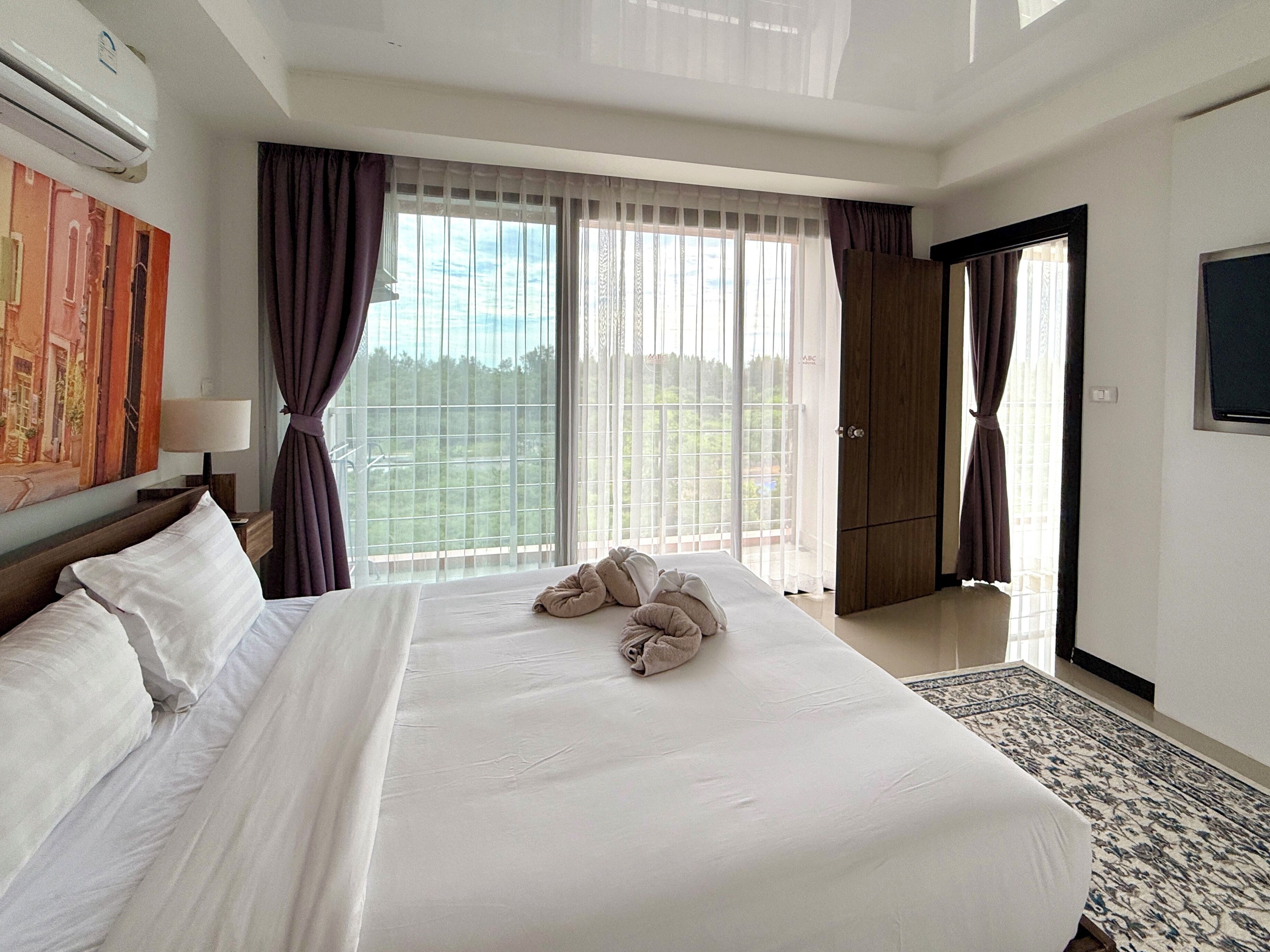 A hotel room with a large bed, a painting on the wall, a window with curtains, and a door leading to a balcony.