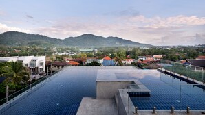 A rooftop infinity pool with a clear view of a town and mountains in the background.