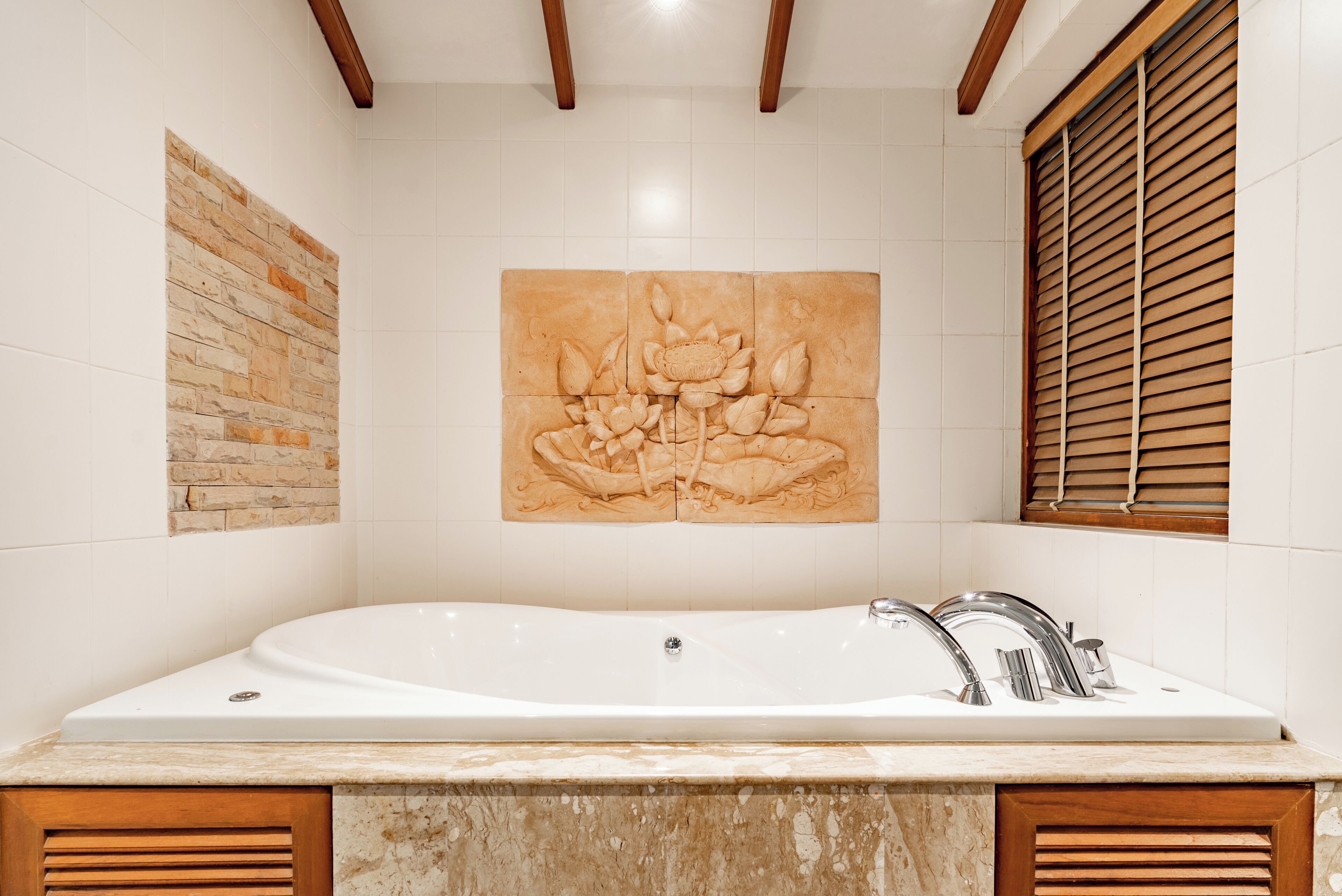 A bathroom with a large bathtub, a wooden window, and a wall-mounted artwork.