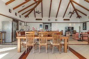 A spacious kitchen with wooden beams, a dining area with a wooden table and chairs, a refrigerator, and a television in the living room. -  Villa Suriya B2 (Patong)