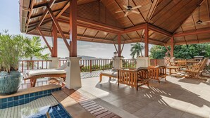 A covered outdoor area with a pool, wooden furniture, and a view of the ocean. -  Villa Suriya B2 (Patong)