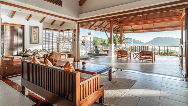 A spacious living area with a wooden bench, a coffee table, and a view of the mountains through a large glass door. -  Villa Suriya B2 (Patong)