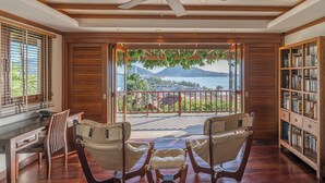A room with a ceiling fan, a wooden bookshelf, a view of the outdoors, and a seating area with chairs. -  Villa Suriya B2 (Patong)