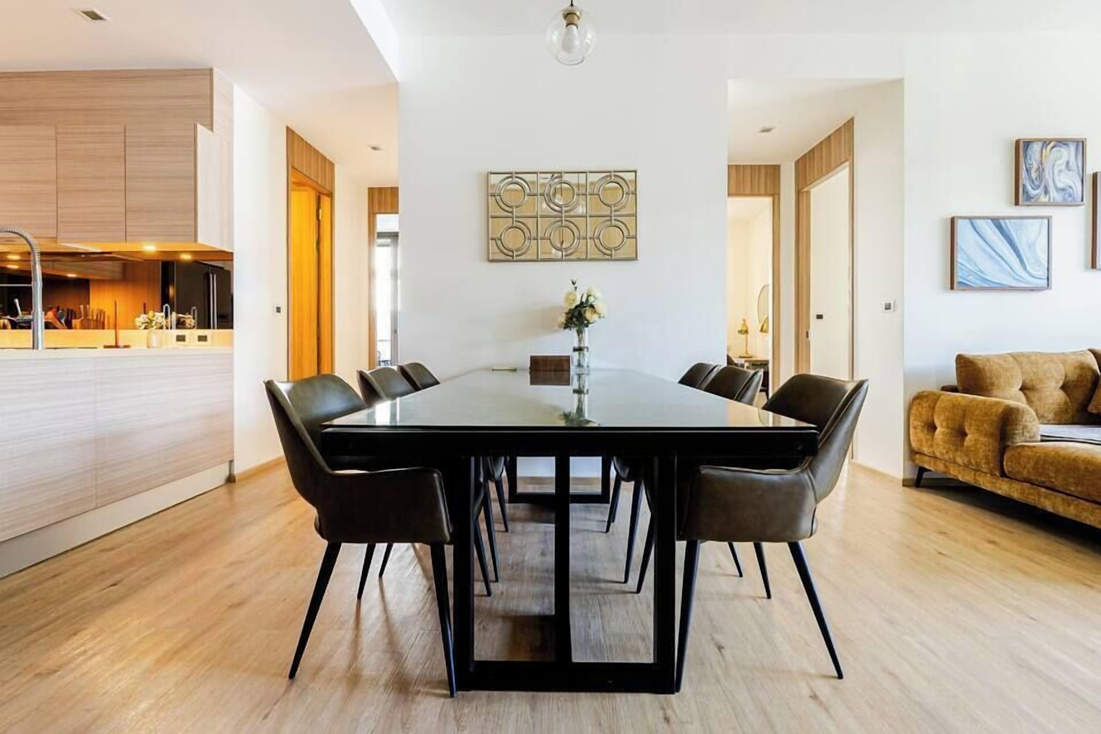 A modern dining area with a large table, six chairs, and a vase of flowers.