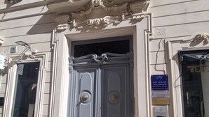 A building with a large, ornate entrance door, a sign indicating an art house, and a visible manhole cover on the sidewalk. - Babuino Apartments - Piazza di Spagna (Rome)