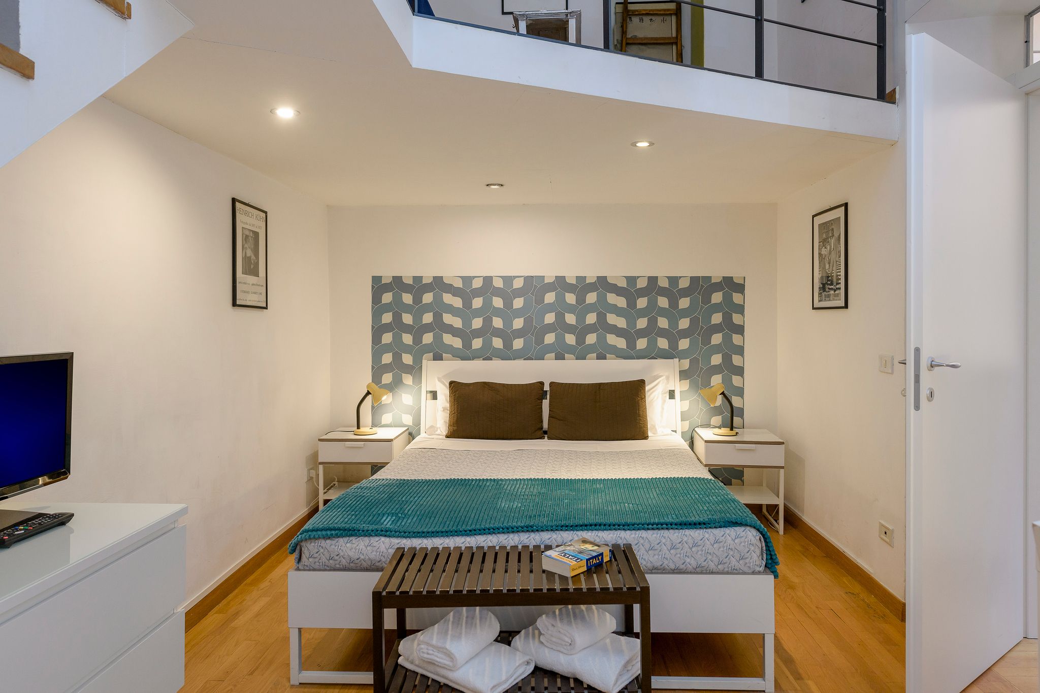 A modern bedroom with a bed, bedside tables, a TV, and a balcony.