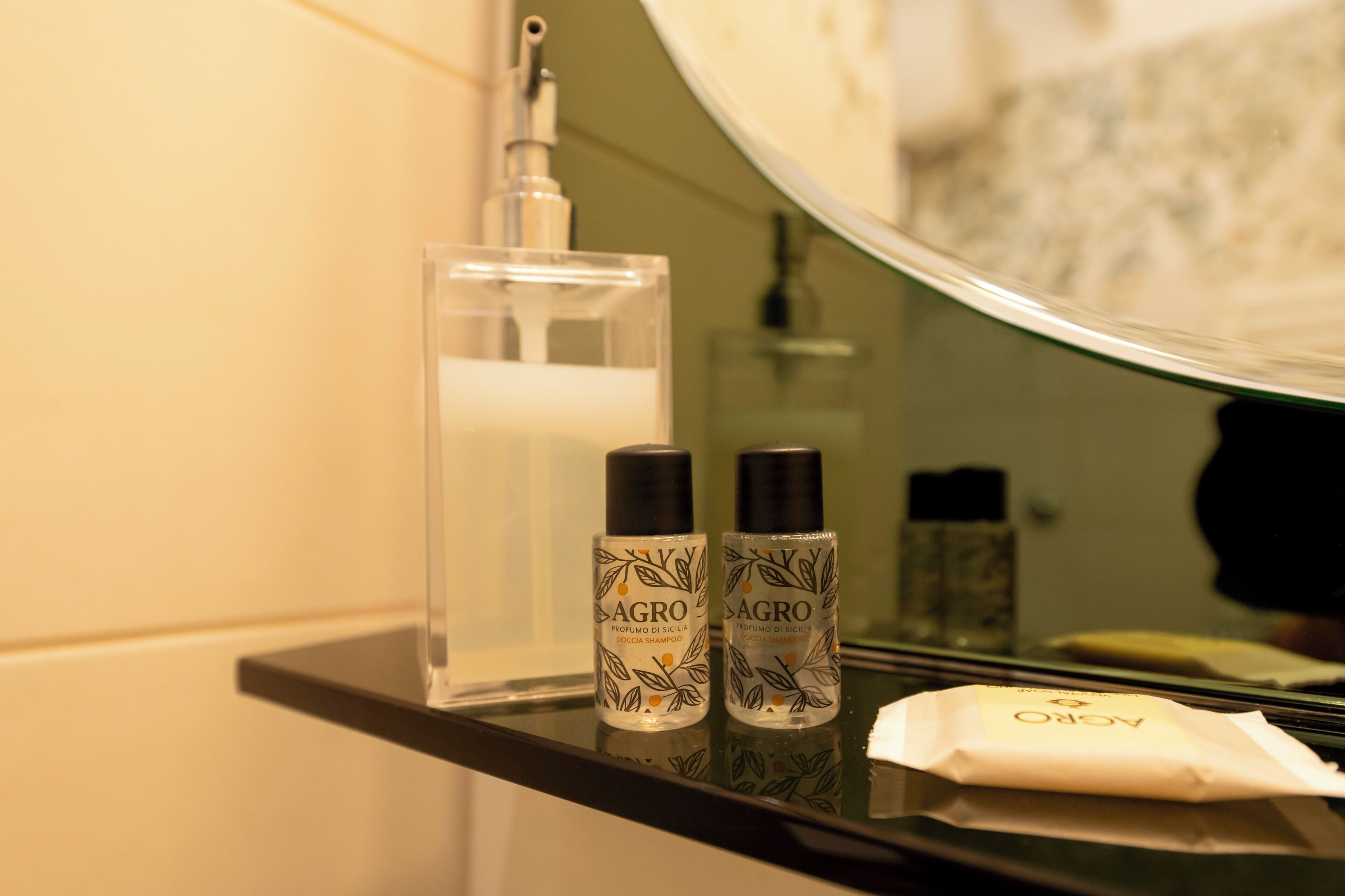A bathroom counter with two bottles of AGRO hair products, a clear bottle of liquid, and a white tissue.