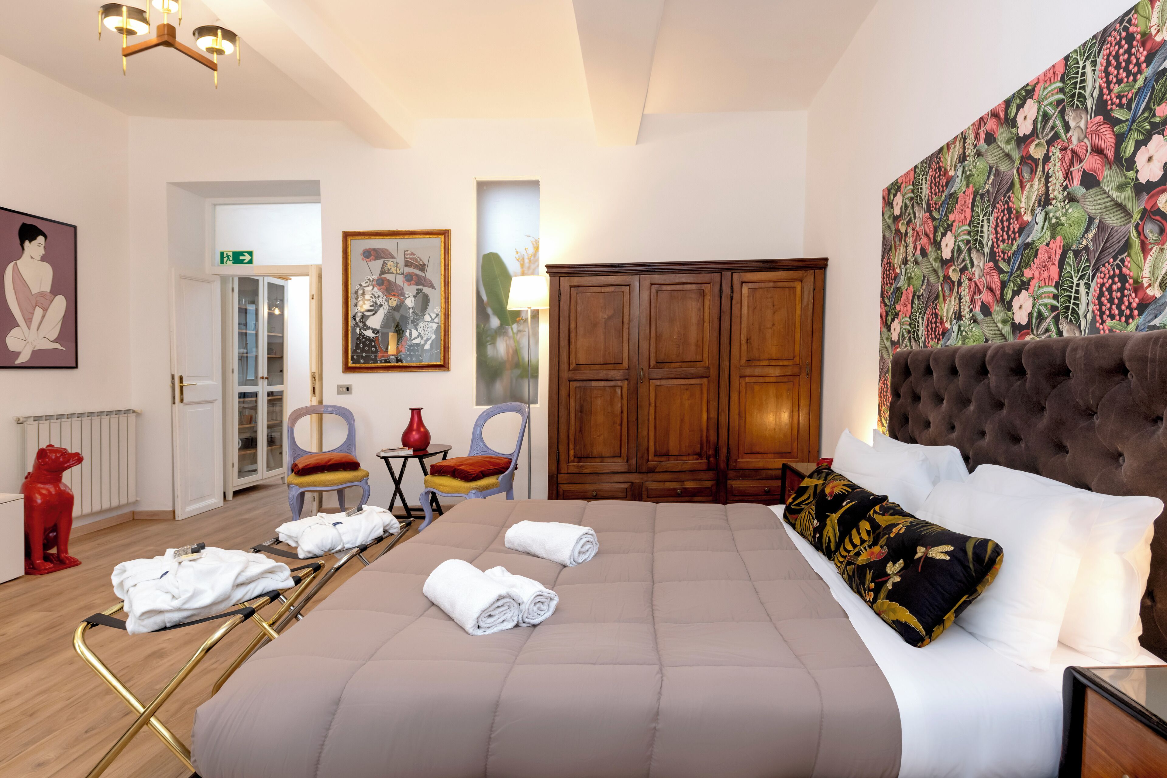 Une chambre d’hôtel avec un grand lit, une armoire en bois, un tableau et une sculpture rouge.