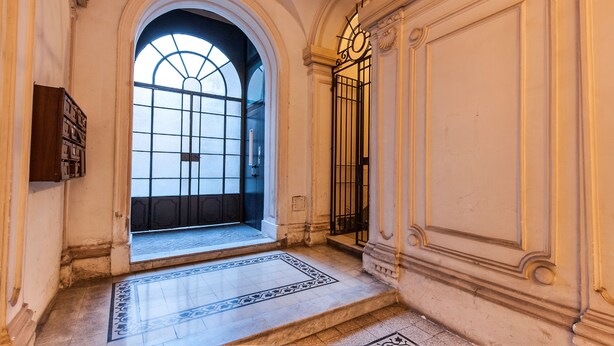 An arched doorway leading to a room with a patterned floor and a view of a window with a grid design. - Babuino Apartments - Piazza di Spagna (Rome)
