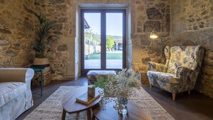 A cozy room with stone walls, a large window, a sofa, a patterned armchair, and a small table with a vase of flowers. - EXCLUSIVE RURAL HOUSE WITH POOL IN LAS RIAS BAIXAS  (MEIS)