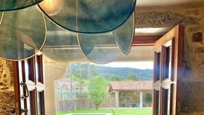 A room with a glass vase on a table, a view of a garden and buildings outside through open doors. - EXCLUSIVE RURAL HOUSE WITH POOL IN LAS RIAS BAIXAS  (MEIS)