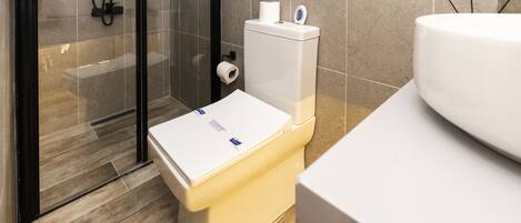 Un baño moderno con inodoro, cabina de ducha de vidrio y lavamanos.