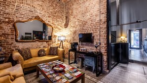 A cozy living room with a brick wall, a sofa, a coffee table with magazines, a TV, and a fireplace. - Selvese Suites – Serviced Living in Galata (Istanbul)