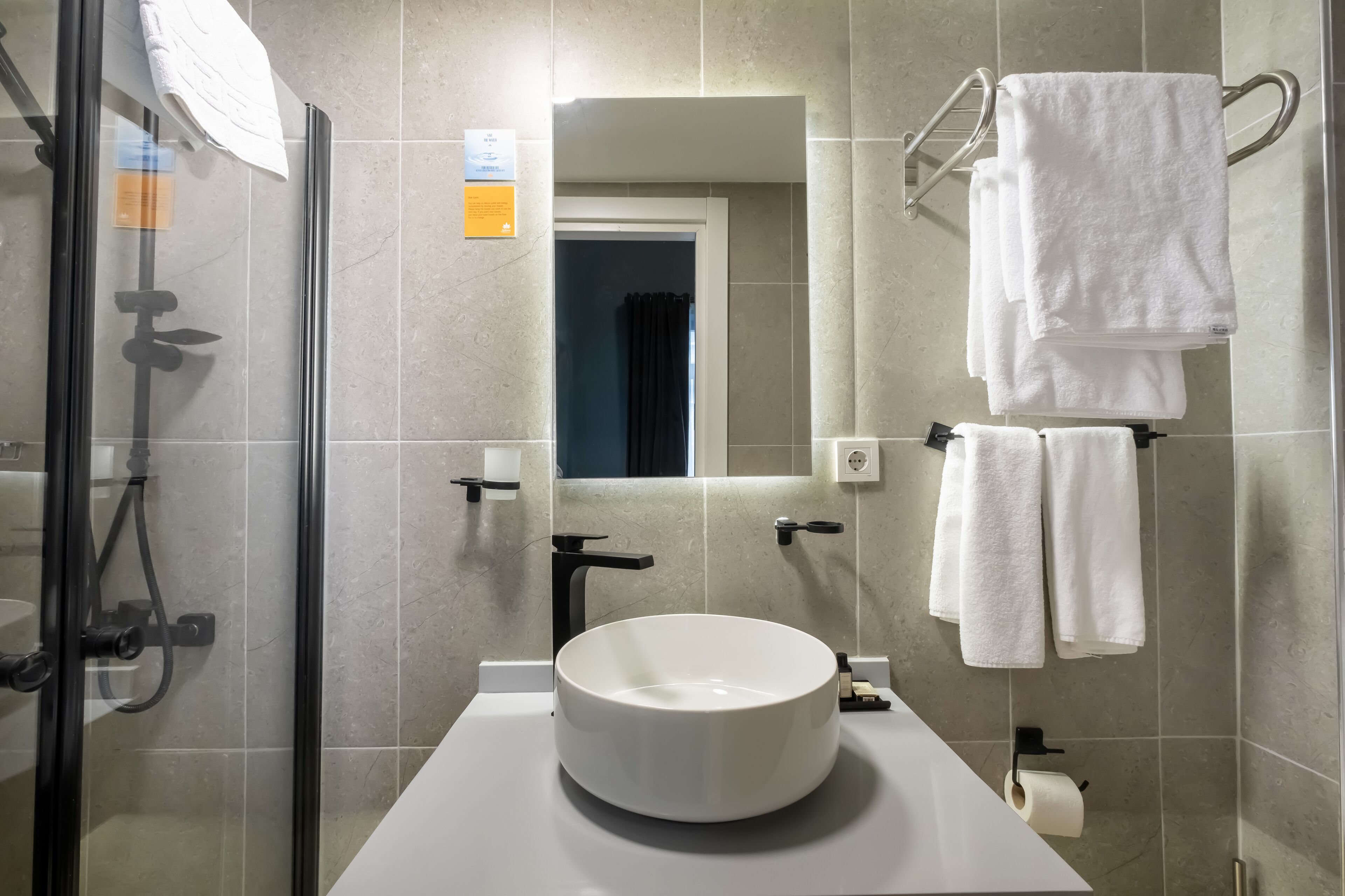 Ein modernes Badezimmer mit einem runden Waschbecken, einer Duschkabine aus Glas und Handtuchhaltern.