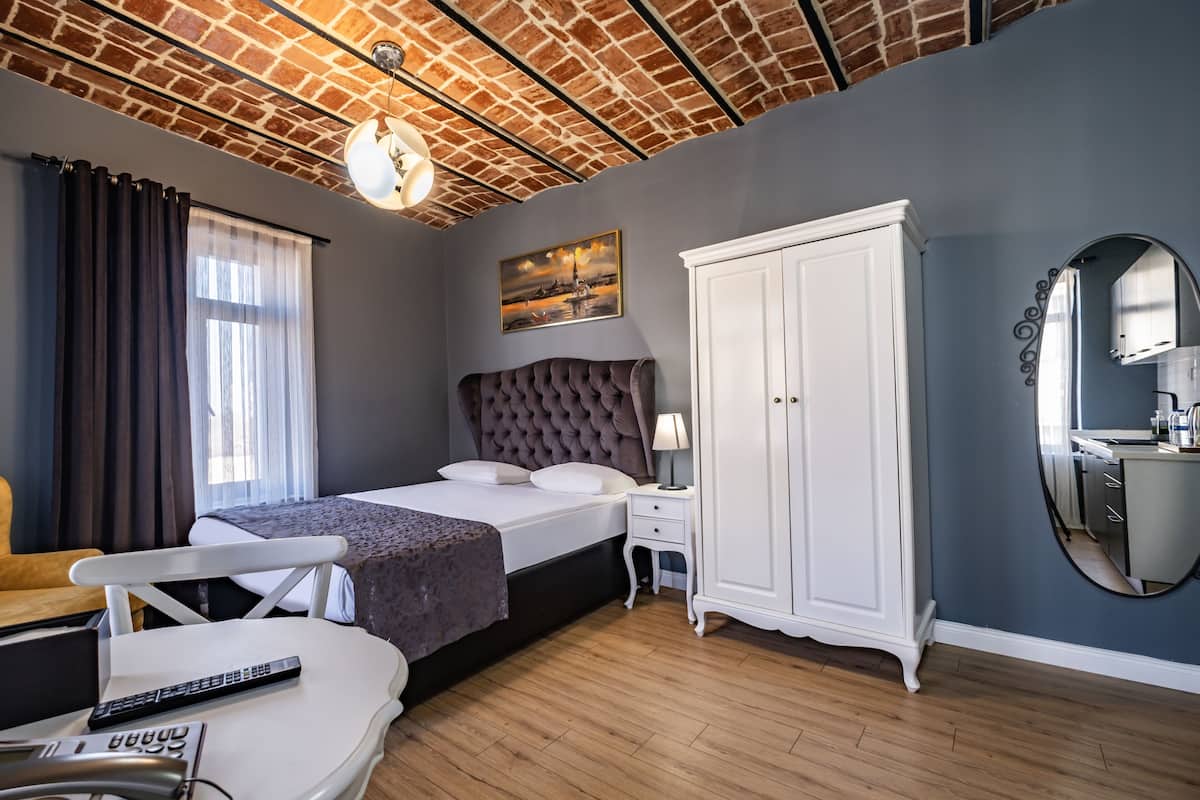 A bedroom with a brick ceiling, a bed, a wardrobe, a bedside table, a chair, and a mirror.