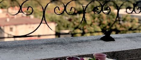A table with a variety of cheeses, fruits, and vegetables on a balcony overlooking a cityscape.