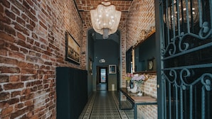 A hallway with brick walls, a patterned floor, a chandelier, and a door with ornate metalwork. - Selvese Suites – Serviced Living in Galata (Istanbul)