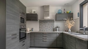 A modern kitchen with a built-in oven, microwave, and stainless steel range hood. There are two wooden cabinets with drawers and a tiled backsplash. - Vacations for 6 around the Gulf (Saint-Gildas-de-Rhuys)