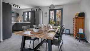 A modern kitchen with dark cabinets, a wooden dining table set for six, and a large window offering a view of the outdoors. - Vacations for 6 around the Gulf (Saint-Gildas-de-Rhuys)